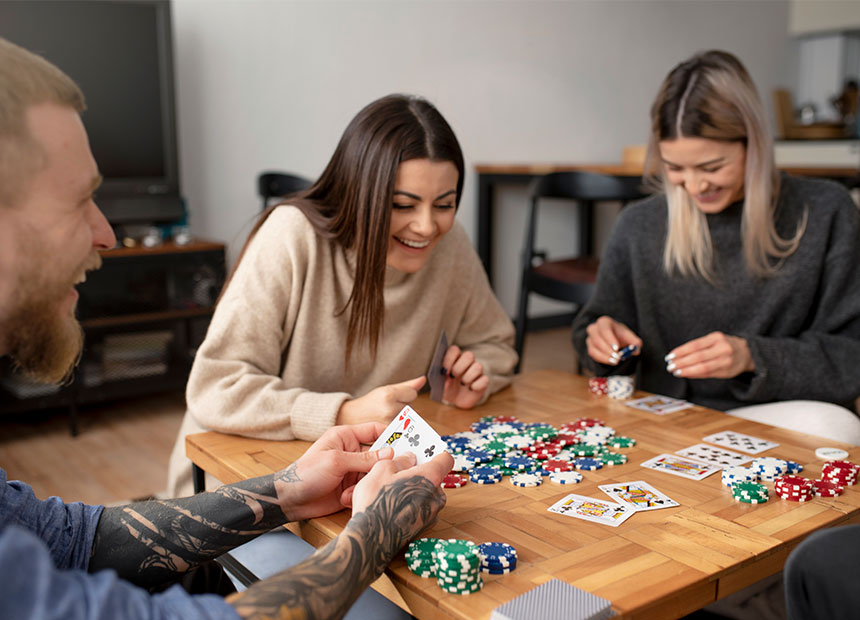 A group of people engaged in a poker game around a wooden table scattered with colorful poker chips and playing cards.